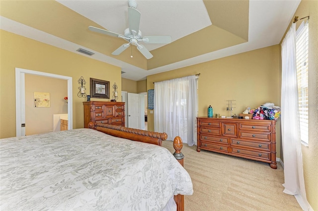 bedroom featuring light carpet, ceiling fan, a tray ceiling, and visible vents