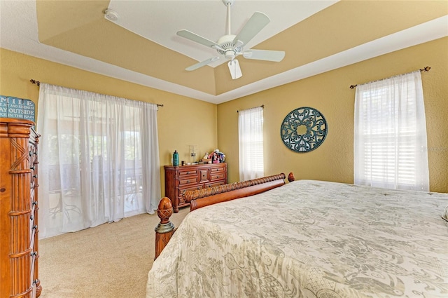 carpeted bedroom with a ceiling fan and a tray ceiling