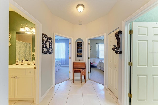 hallway featuring baseboards, light colored carpet, a sink, and light tile patterned flooring