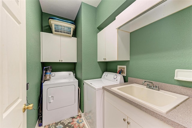 clothes washing area featuring cabinet space, a textured wall, a sink, and washing machine and clothes dryer