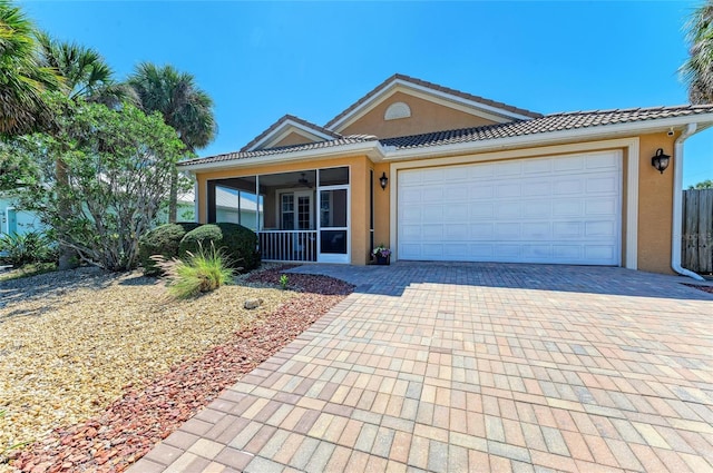 ranch-style house with decorative driveway, a tile roof, stucco siding, an attached garage, and a sunroom