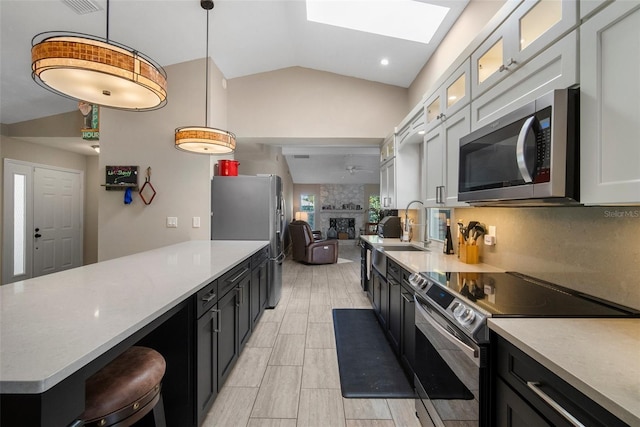 kitchen with lofted ceiling with skylight, a fireplace, stainless steel appliances, and light countertops