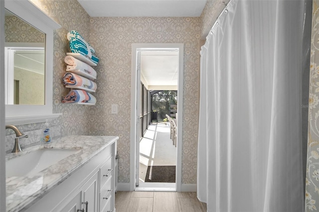 bathroom with baseboards, vanity, and wallpapered walls