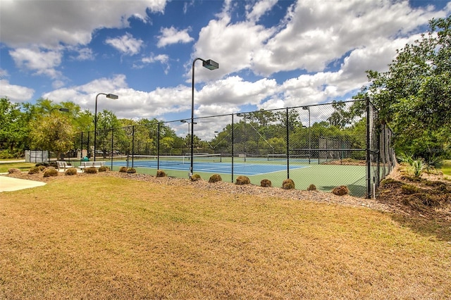 view of tennis court featuring a lawn and fence