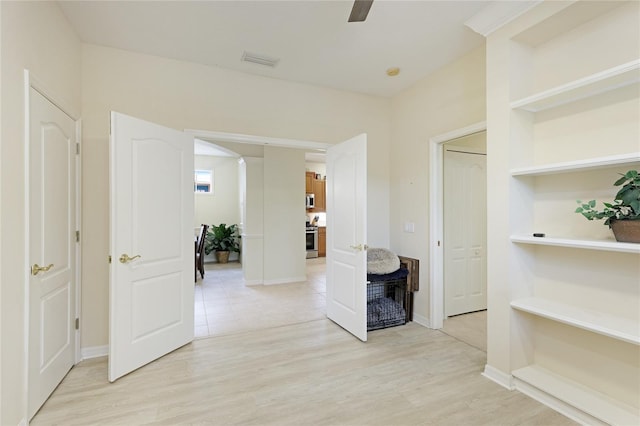 hallway featuring arched walkways, visible vents, baseboards, and light wood-style floors