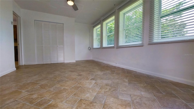 empty room featuring ceiling fan, stone finish flooring, and baseboards