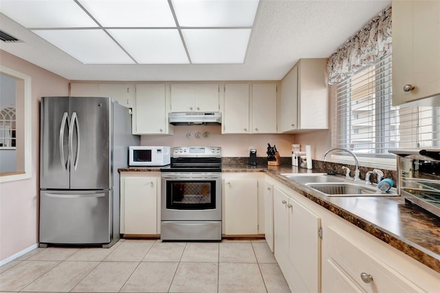 kitchen with stainless steel appliances, dark countertops, a sink, and under cabinet range hood