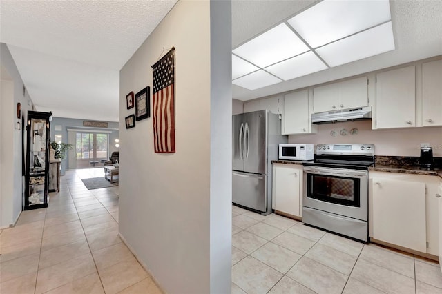 kitchen with light tile patterned floors, stainless steel appliances, dark countertops, a textured ceiling, and under cabinet range hood