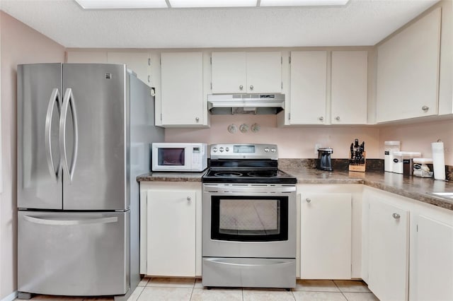 kitchen with a textured ceiling, light tile patterned flooring, under cabinet range hood, appliances with stainless steel finishes, and dark countertops