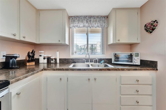 kitchen with dark countertops, a toaster, white cabinetry, and a sink