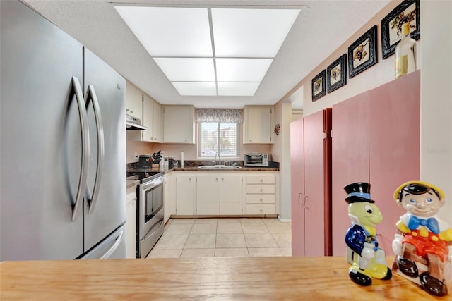 kitchen featuring light tile patterned flooring, under cabinet range hood, stainless steel appliances, a sink, and dark countertops