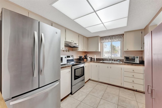 kitchen featuring a toaster, dark countertops, stainless steel appliances, under cabinet range hood, and a sink