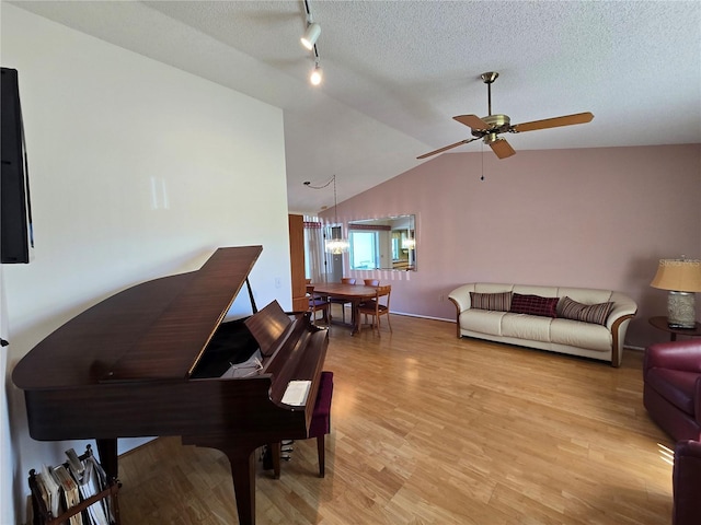 living room with a textured ceiling, ceiling fan, lofted ceiling, light wood finished floors, and rail lighting