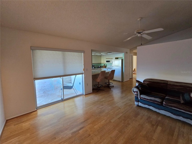 living area with a textured ceiling, vaulted ceiling, light wood-type flooring, and a ceiling fan