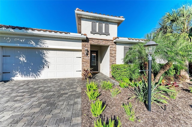 view of front facade with stucco siding, decorative driveway, stone siding, an attached garage, and a tiled roof