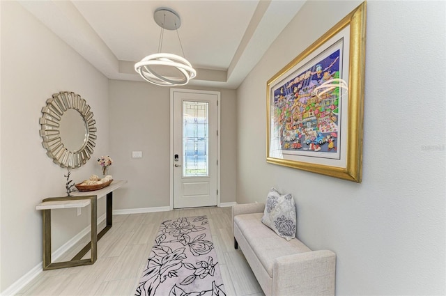 doorway to outside featuring baseboards, a raised ceiling, a chandelier, and light wood finished floors