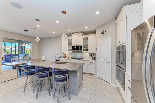 kitchen featuring a breakfast bar area, decorative backsplash, white cabinets, stainless steel appliances, and a sink