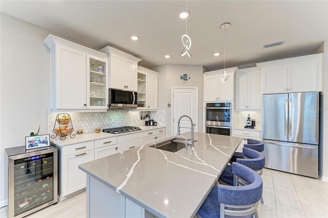 kitchen with beverage cooler, visible vents, a sink, stainless steel appliances, and a kitchen bar