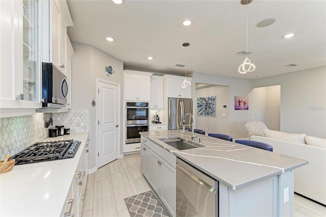 kitchen with a kitchen island with sink, a sink, tasteful backsplash, open floor plan, and appliances with stainless steel finishes