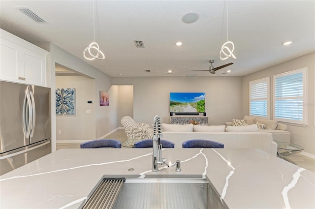 kitchen featuring visible vents, freestanding refrigerator, hanging light fixtures, white cabinetry, and open floor plan