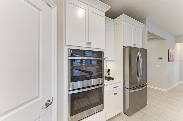 kitchen with wood finish floors, stainless steel appliances, white cabinets, light countertops, and baseboards