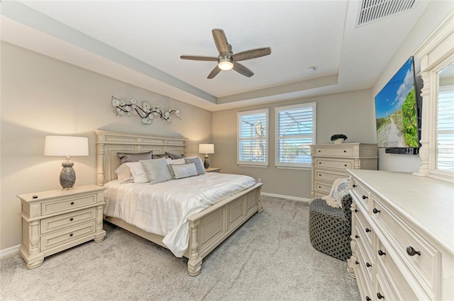 bedroom with a tray ceiling, multiple windows, visible vents, and light carpet