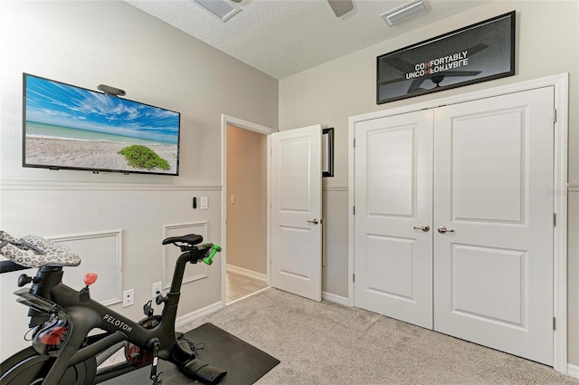 exercise area featuring baseboards, light colored carpet, visible vents, and a textured ceiling