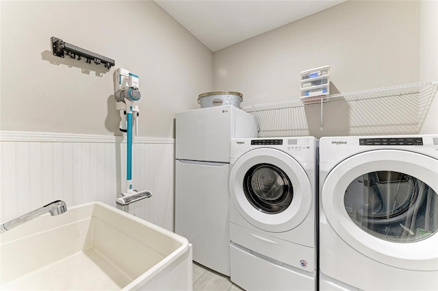 clothes washing area featuring laundry area, separate washer and dryer, a wainscoted wall, and a sink