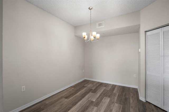 unfurnished room featuring a textured ceiling, dark wood-style flooring, visible vents, baseboards, and an inviting chandelier