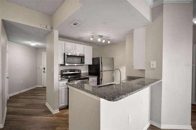 kitchen featuring white cabinets, appliances with stainless steel finishes, dark wood-style flooring, a peninsula, and a sink