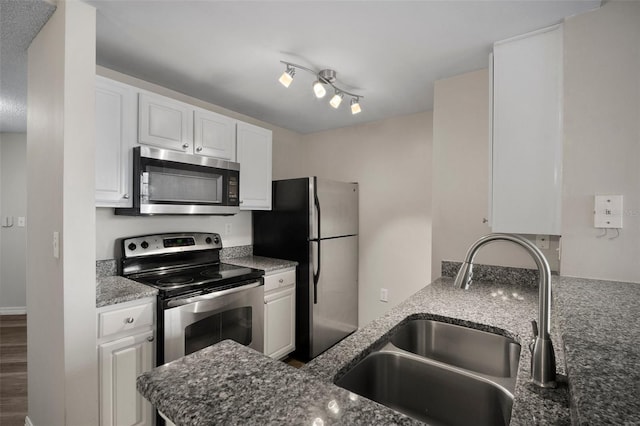 kitchen featuring dark stone counters, appliances with stainless steel finishes, a sink, and white cabinets