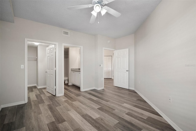 unfurnished bedroom with a textured ceiling, wood finished floors, visible vents, baseboards, and a spacious closet