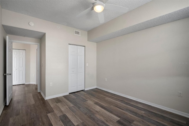 unfurnished bedroom with baseboards, visible vents, dark wood-style flooring, a textured ceiling, and a closet