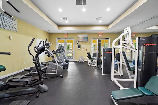 gym featuring a tray ceiling, visible vents, and baseboards