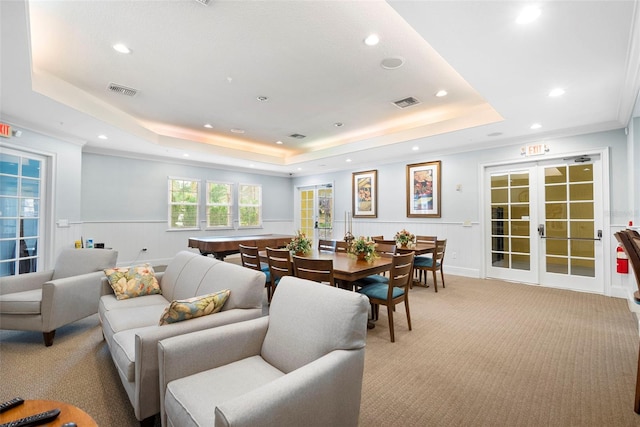 living area with a raised ceiling, wainscoting, light carpet, and french doors