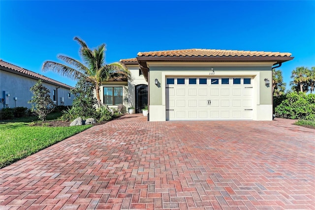 mediterranean / spanish house with a garage, decorative driveway, a tile roof, and stucco siding