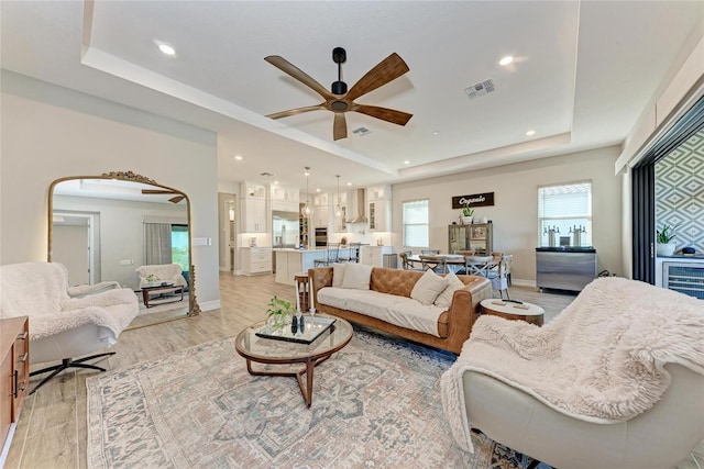 living room with a tray ceiling, light wood-type flooring, visible vents, and baseboards