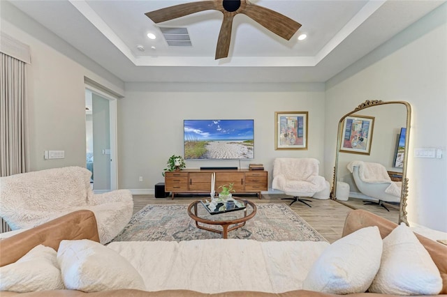 living area with a tray ceiling, wood finished floors, and recessed lighting