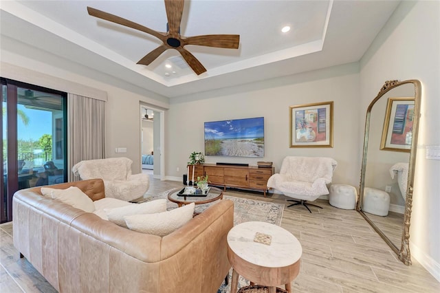 living area with a tray ceiling, light wood-type flooring, recessed lighting, and baseboards