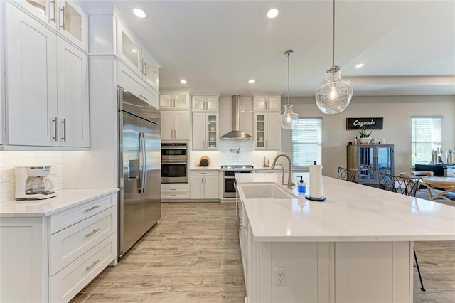 kitchen with stainless steel appliances, white cabinets, a sink, and wall chimney range hood