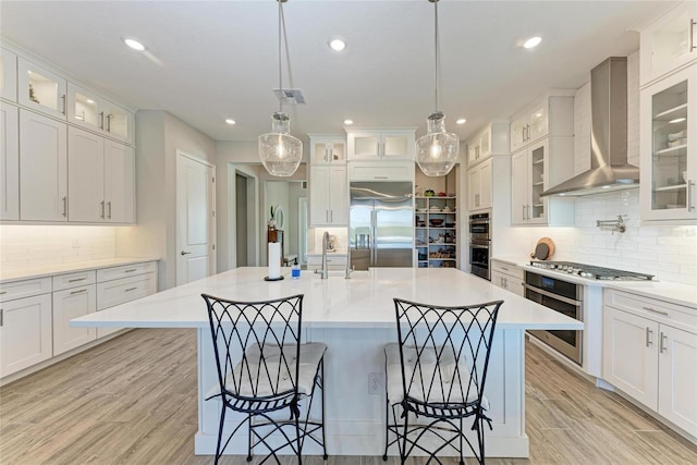 kitchen with light wood finished floors, light countertops, appliances with stainless steel finishes, a sink, and wall chimney range hood