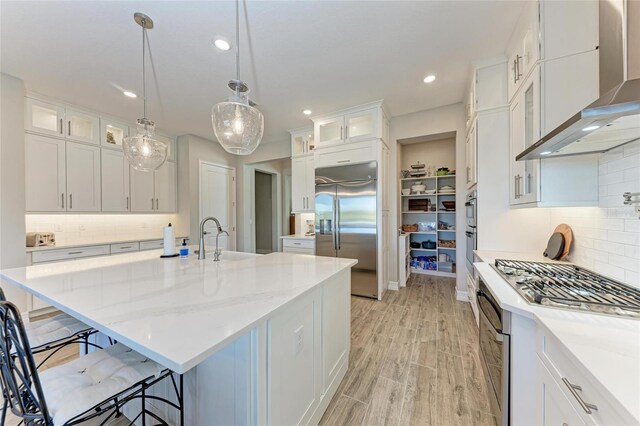 kitchen with stainless steel appliances, a sink, a kitchen breakfast bar, wall chimney exhaust hood, and light wood finished floors