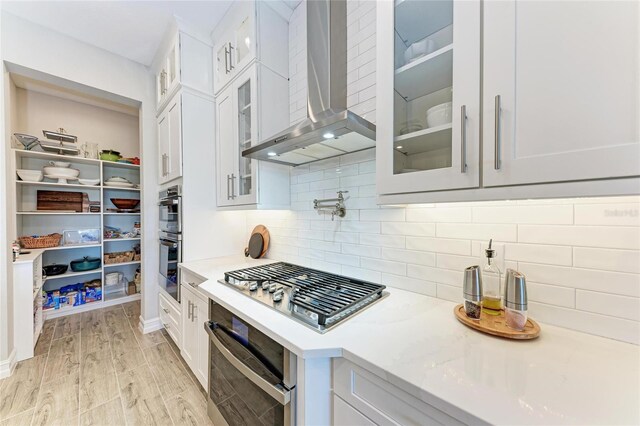 kitchen with stainless steel appliances, white cabinets, decorative backsplash, and wall chimney exhaust hood