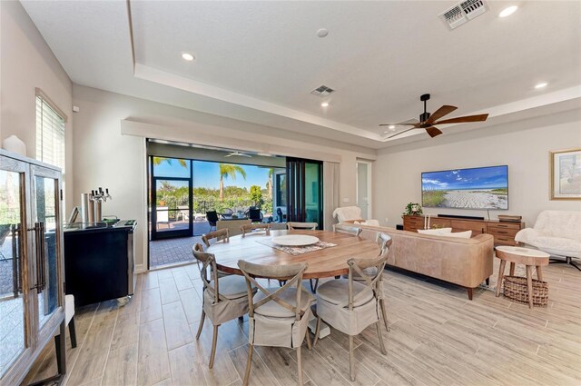 dining space featuring wood tiled floor, visible vents, a raised ceiling, and a wealth of natural light