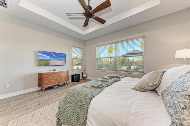 bedroom featuring light wood-style floors, a tray ceiling, ceiling fan, and baseboards