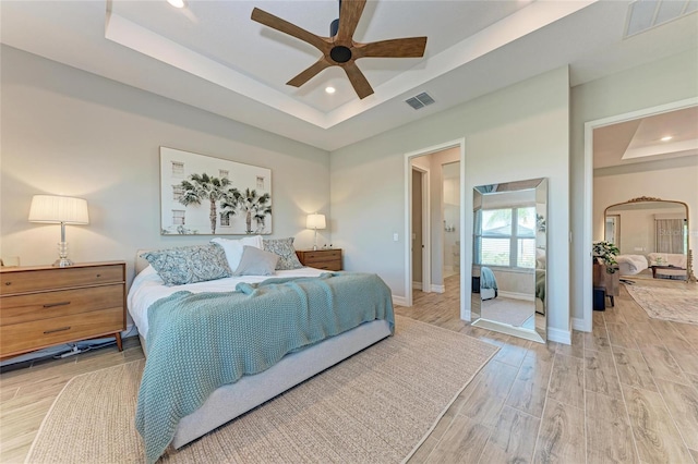 bedroom with a raised ceiling, visible vents, baseboards, and light wood finished floors