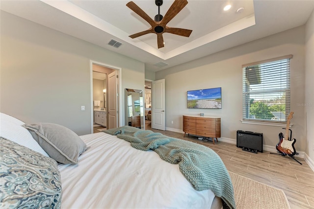 bedroom featuring a raised ceiling, visible vents, wood tiled floor, ensuite bath, and baseboards