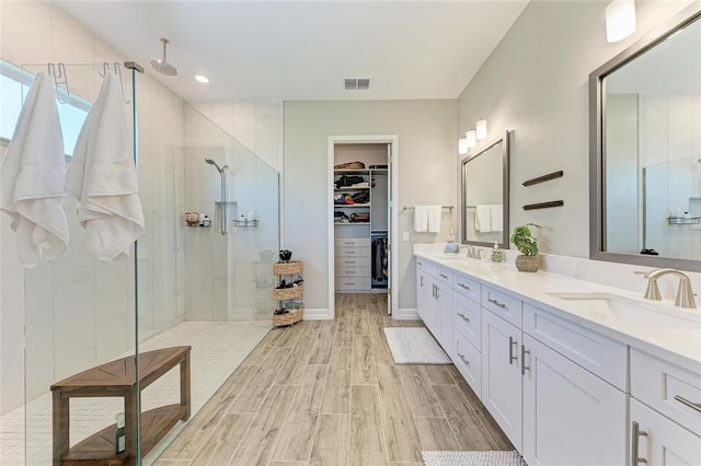 full bath with double vanity, visible vents, a stall shower, wood tiled floor, and a sink