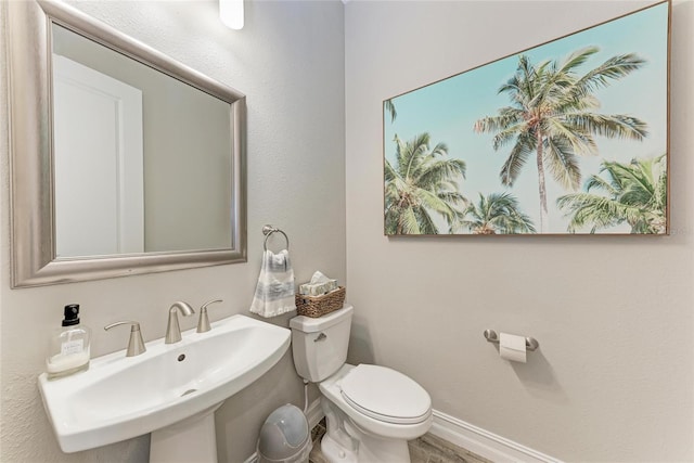 bathroom featuring toilet, baseboards, and a sink