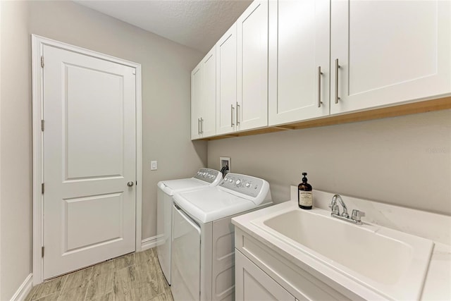 washroom featuring cabinet space, light wood-style flooring, a sink, a textured ceiling, and washer and dryer